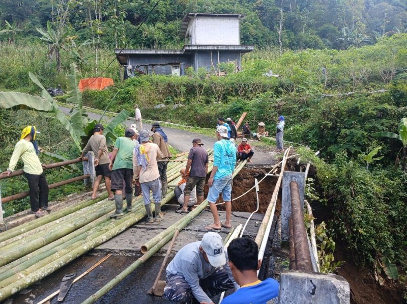 Warga bergotong royong membangun jembatan darurat dari bambu agar pejalan kaki dan roda dua tetap bisa lewat.