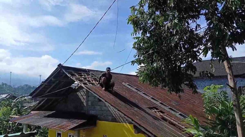 Warga melakukan perbaikan atap yang rusak terkena angin kencang.